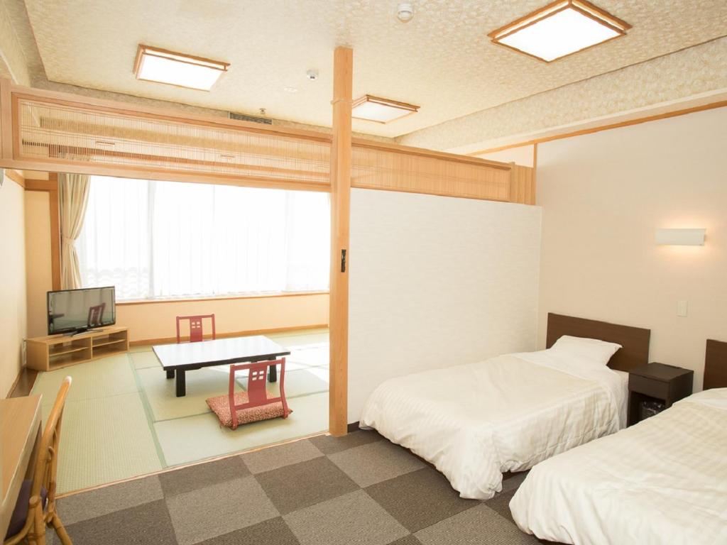 Cette chambre comprend deux lits, une table et une télévision. dans l'établissement Itoen Hotel Iizakakanouya, à Fukushima