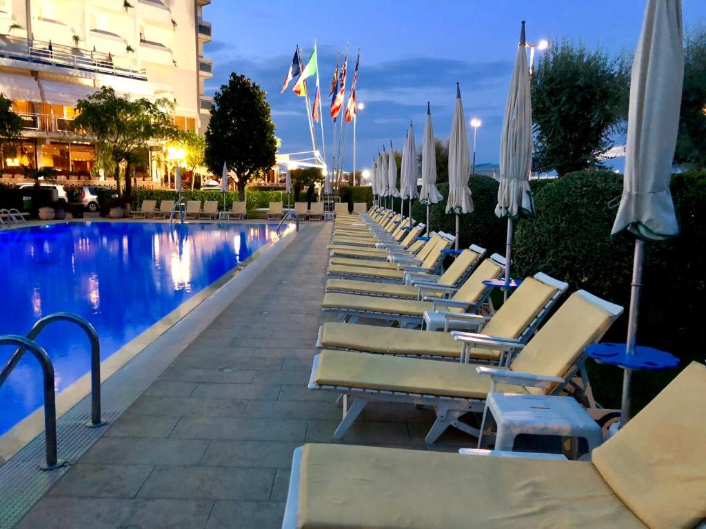 une rangée de chaises et de parasols à côté d'une piscine dans l'établissement Hotel Bristol, à Sottomarina