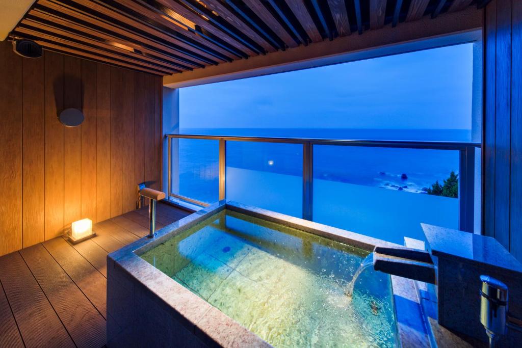 une baignoire dans une pièce avec une grande fenêtre dans l'établissement Hamanoyu, à Higashiizu
