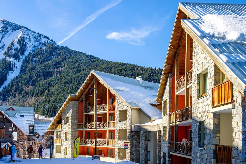 un groupe de bâtiments dans la neige à côté d'une montagne dans l'établissement Résidence Capfun Couleurs Soleil, Oz en Oisans, à Oz