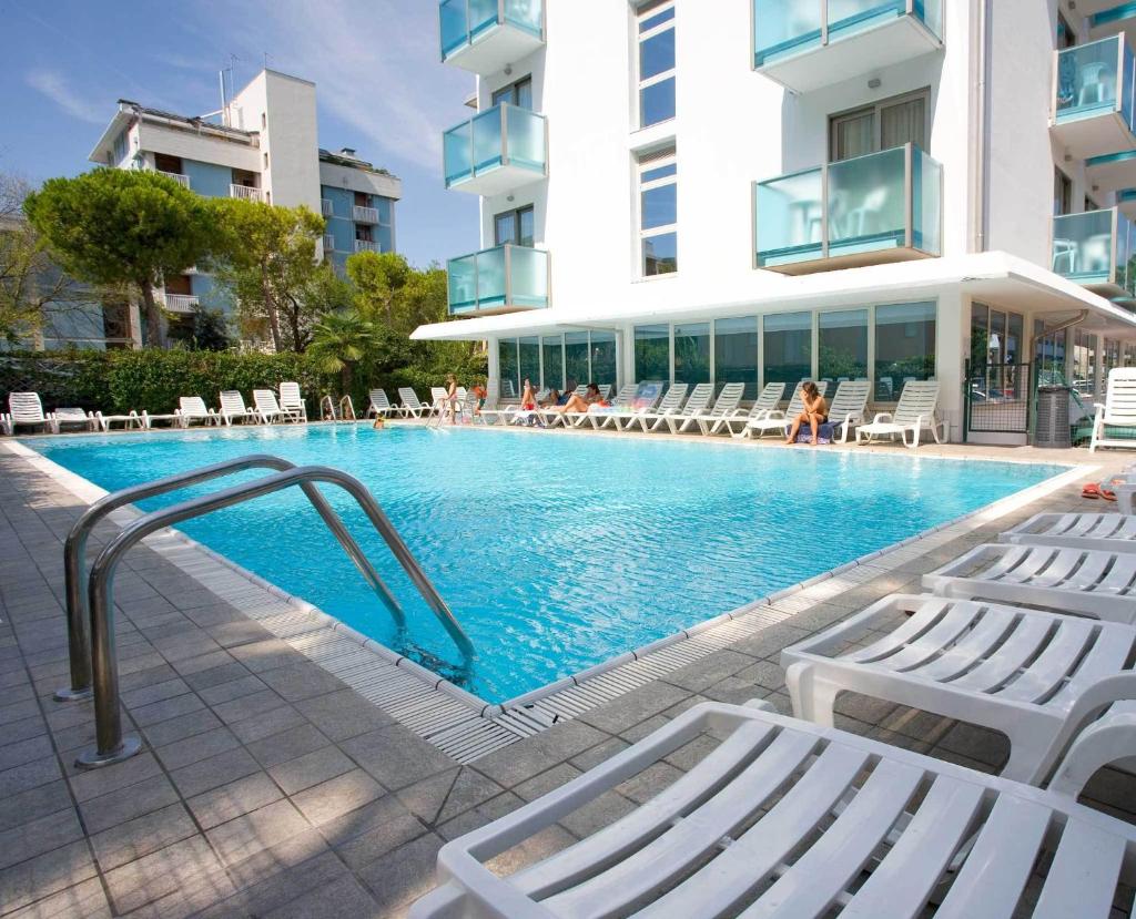 une piscine avec des chaises blanches et un bâtiment dans l'établissement Hotel Katja, à Bibione