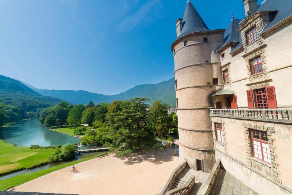 un château avec une rivière et des montagnes en arrière-plan dans l'établissement L'imprévu, à Vaulnaveys-le-Bas