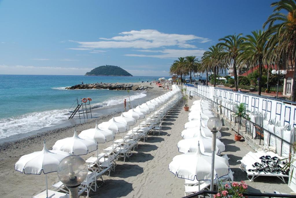 une rangée de parasols et de chaises blanches sur une plage dans l'établissement Hotel Marisa, à Albenga