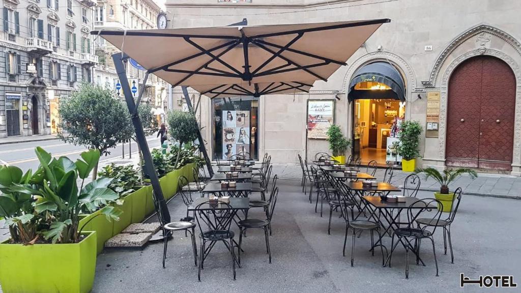 un groupe de tables et de chaises avec un parasol dans une rue dans l'établissement Hotel Youri Il Magnifico, à Gênes