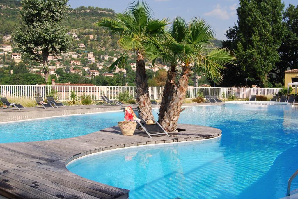 une femme assise sur une chaise à côté d'une piscine avec deux palmiers dans l'établissement Résidence Lagrange Vacances - Les Cottages Varois, à Solliès-Toucas