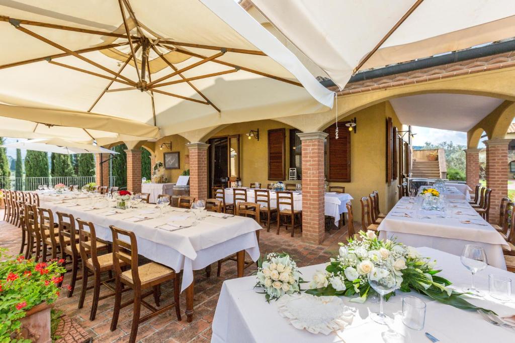 un restaurant avec des tables blanches, des chaises et des parasols dans l'établissement VILLA LIGUSTRO, à Riparbella