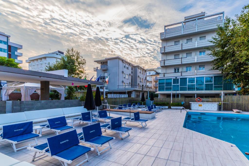une piscine avec des chaises bleues et un bâtiment dans l'établissement Eurhotel, à Rimini
