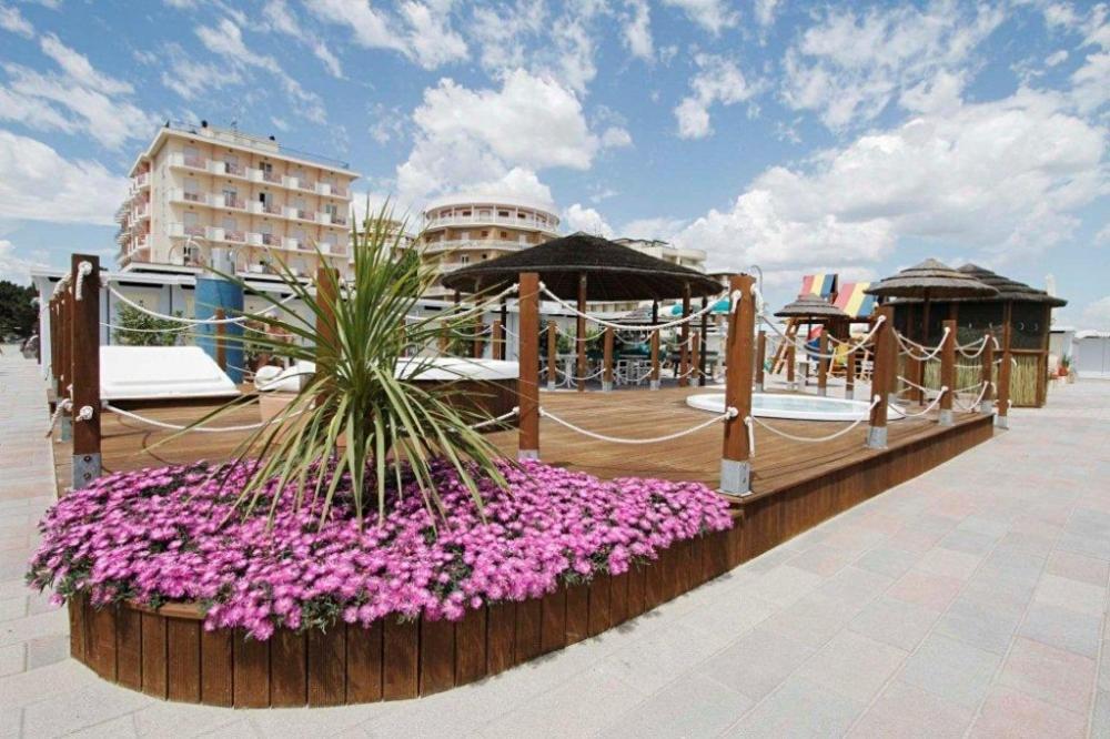 une terrasse avec des fleurs roses et des parasols sur une plage dans l'établissement Hotel Torremaura, à Milano Marittima