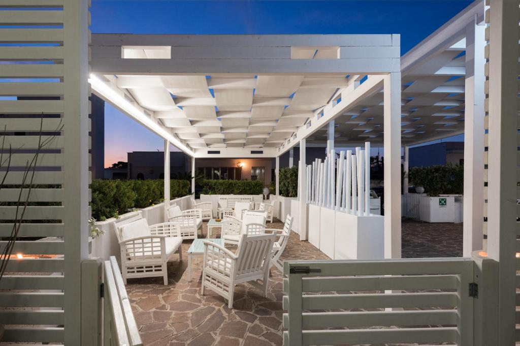 un patio avec des chaises et des tables blanches sous une pergola dans l'établissement Hotel Luna Lido, à Torre San Giovanni