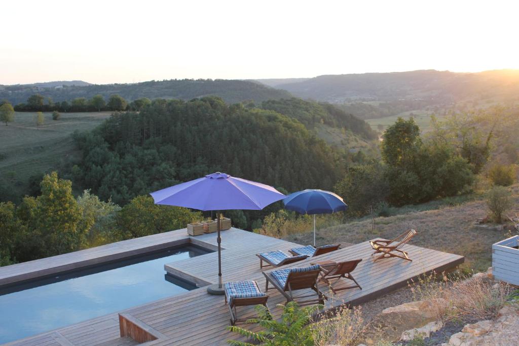 une piscine avec deux parasols et deux chaises ainsi qu'une terrasse avec dans l'établissement Les Terrasses de Labade Gite, à Coubisou