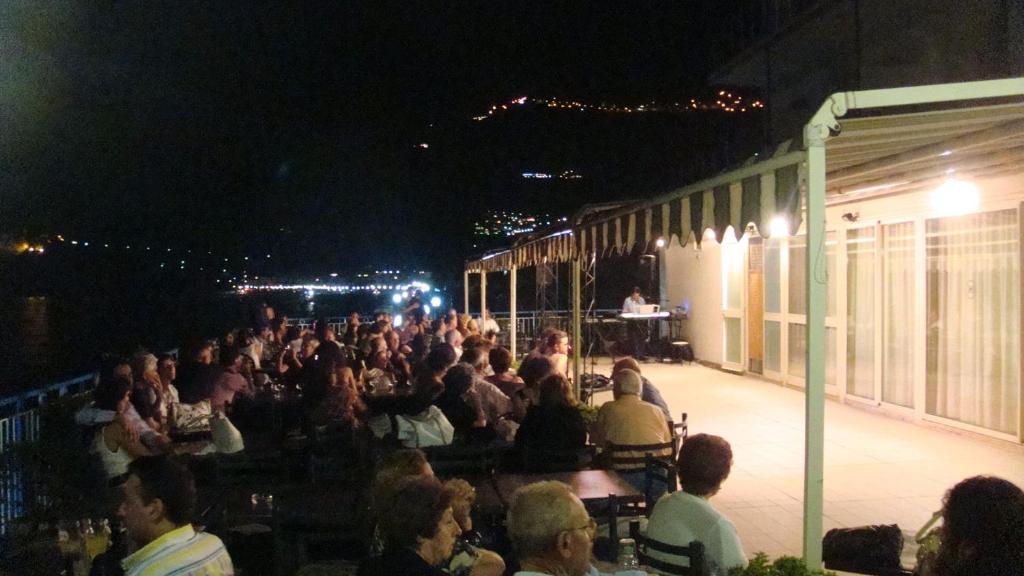 une foule assise sur une terrasse la nuit dans l'établissement Hotel Kennedy, à SantʼAlessio Siculo