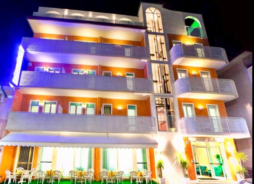 un grand bâtiment avec des tables et des chaises devant lui dans l'établissement Hotel Erika, à Caorle