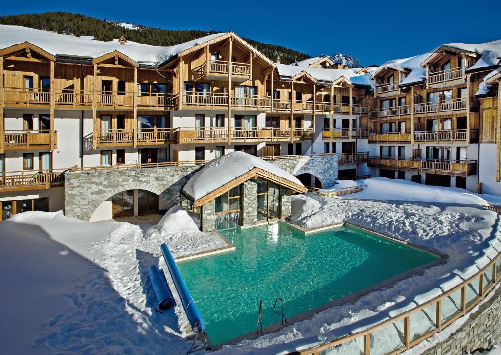 un complexe avec une piscine dans la neige dans l'établissement Résidence Club mmv Le Hameau des Airelles ****, à Montgenèvre