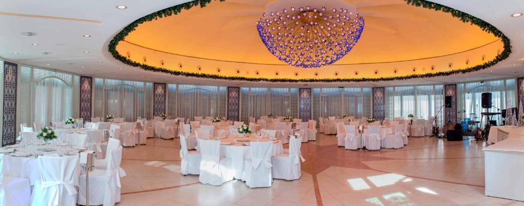 une salle de banquet avec des tables blanches et un grand lustre dans l'établissement Hotel Oasi Di Kufra, à Sabaudia 100 autres photos
