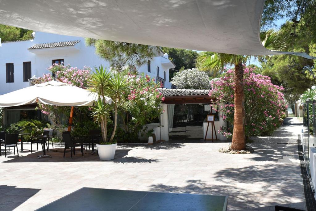 un patio avec des tables et des chaises, des arbres et des fleurs dans l'établissement Hotel Gabbiano Beach, à Vieste