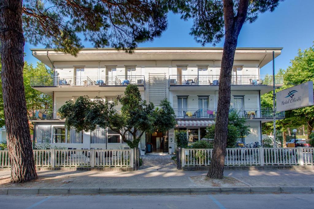 un bâtiment blanc avec une clôture blanche et des arbres dans l'établissement HOTEL OLIVER, à Cervia