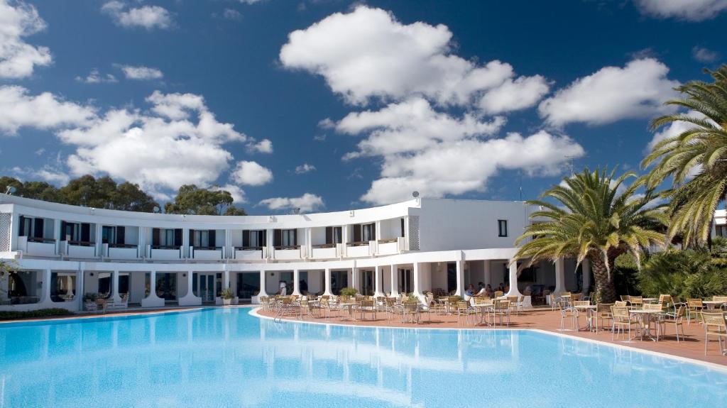 un grand bâtiment blanc avec une grande piscine dans l'établissement Hotel Flamingo, à Santa Margherita di Pula