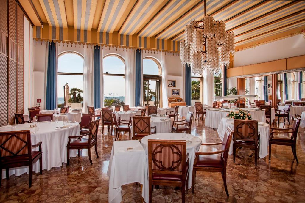 une salle à manger avec tables et chaises et un lustre dans l'établissement Hotel Excelsior Venice, sur le Lido de Venise