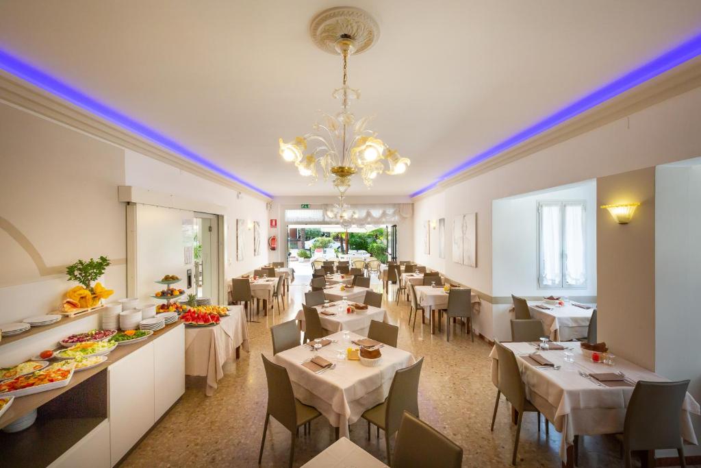 un restaurant avec des tables et des chaises blanches et un lustre dans l'établissement Hotel Atenea Golden Star, à Caorle