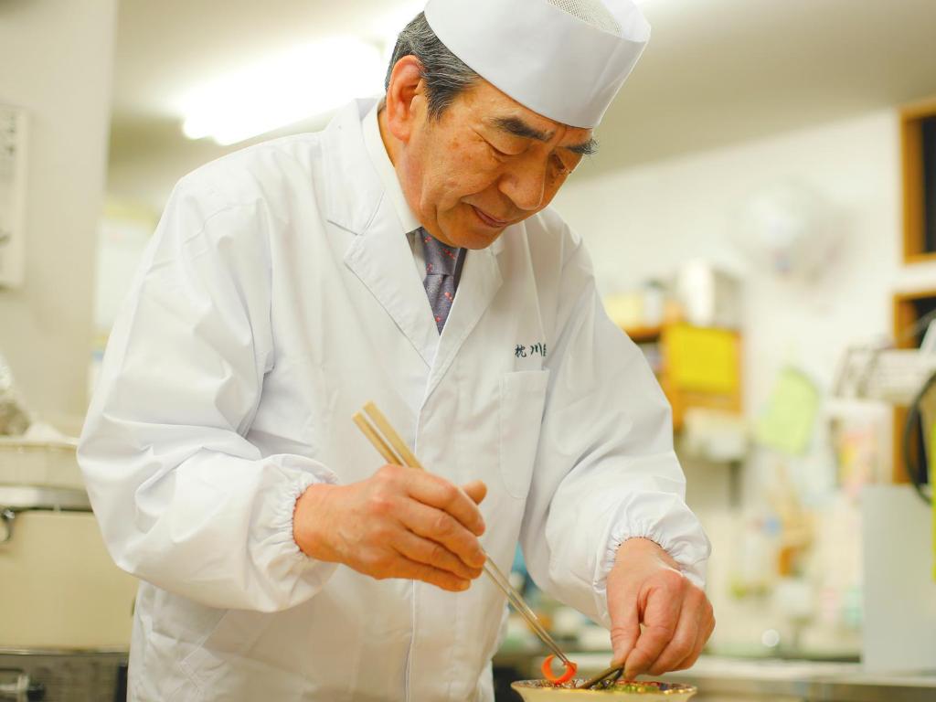 un homme dans une cuisine préparant de la nourriture avec des baguettes dans l'établissement Ryokan Chinsen-Rou, à Nantan city