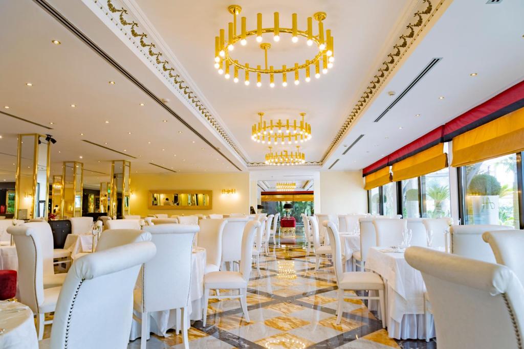 une salle à manger avec des chaises blanches et des lustres dans l'établissement Hotel Ariston, à Paestum