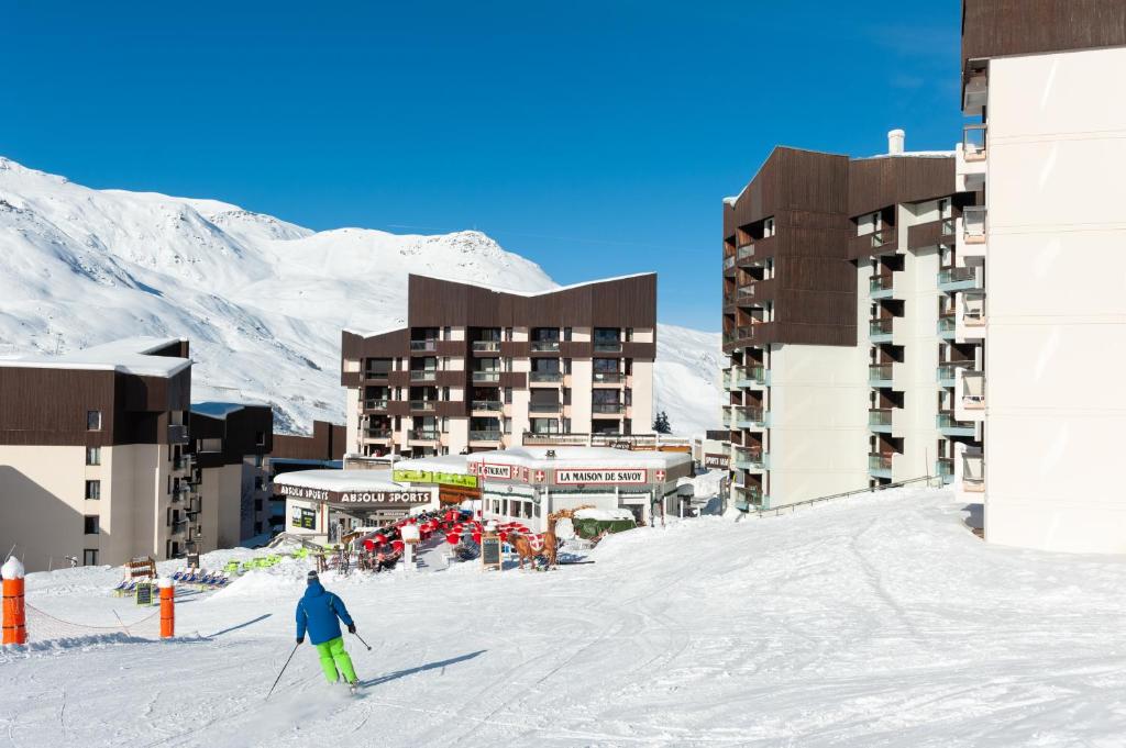 une personne à skis dans la neige devant un hôtel dans l'établissement Résidence Pierre & Vacances Les Combes, aux Menuires
