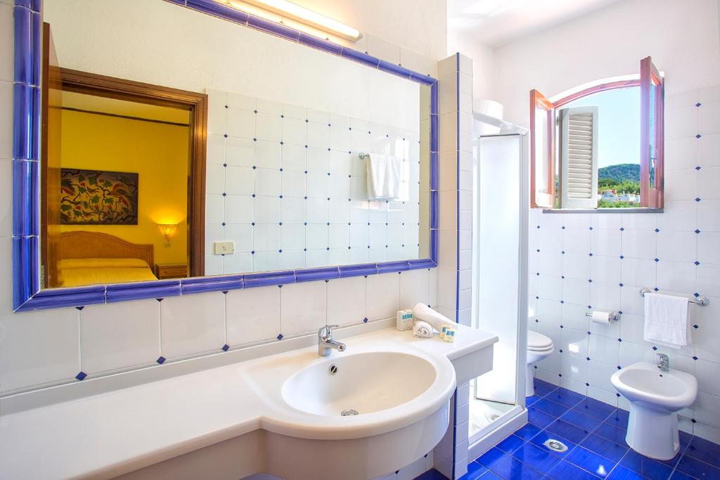 une salle de bain avec un lavabo, des toilettes et un miroir dans l'établissement Hotel La Scogliera, à Ischia