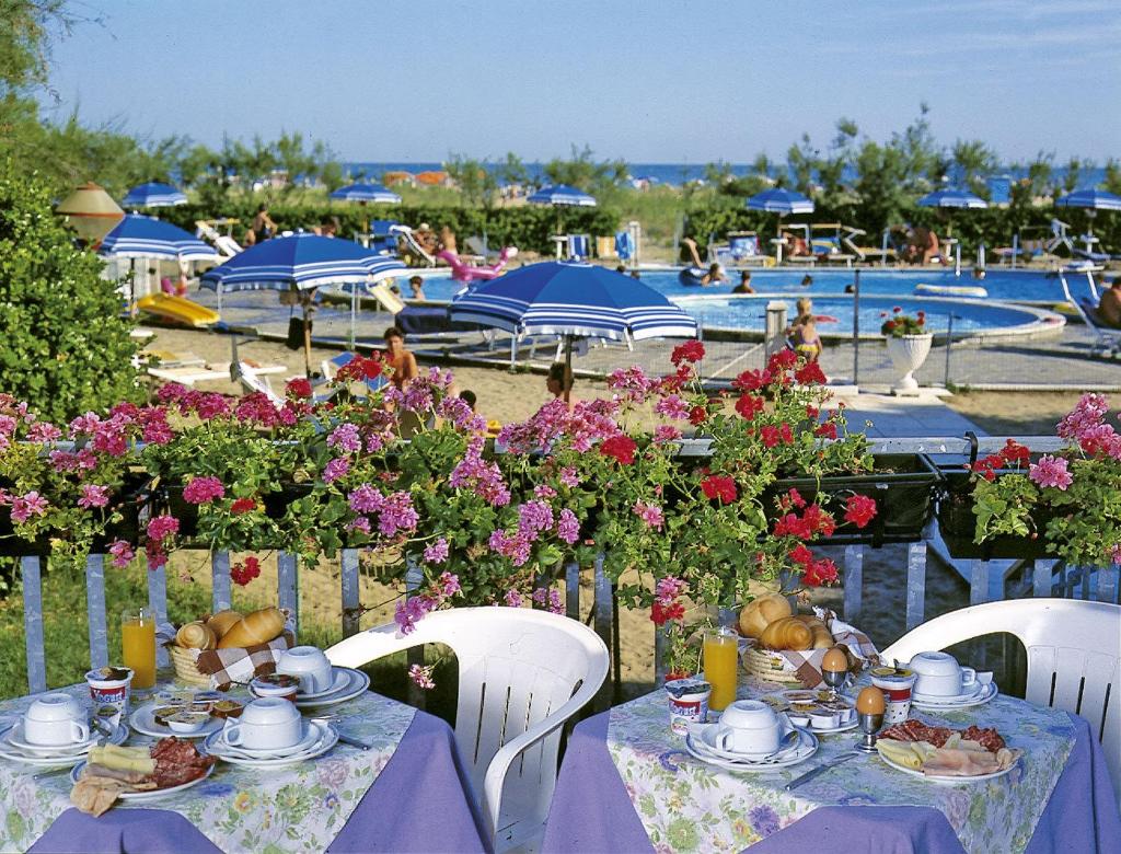 - une table avec des assiettes de nourriture et des fleurs et une piscine dans l'établissement Hotel Bertha Fronte Mare, à Lido di Jesolo