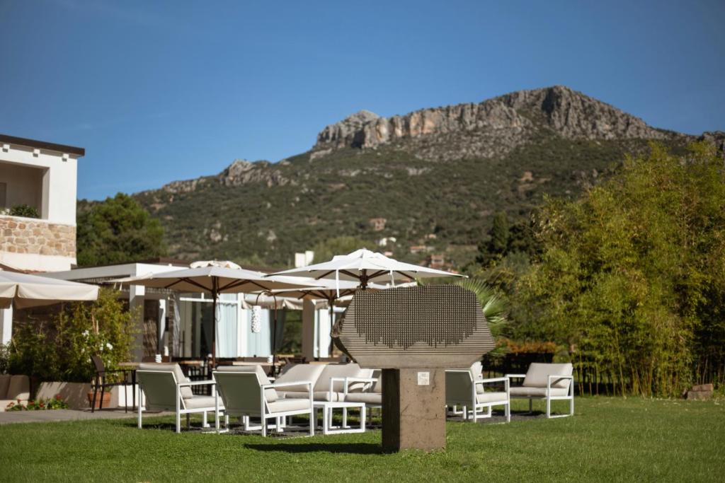 un groupe de chaises et de parasols avec une montagne en arrière-plan dans l'établissement Lanthia Resort, à Santa Maria Navarrese