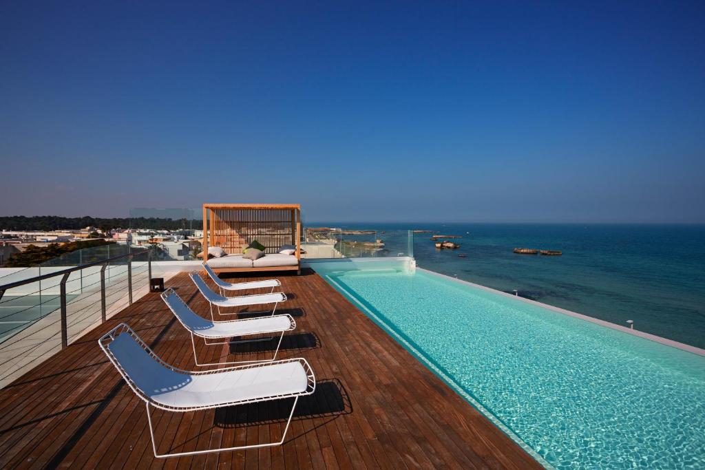 une piscine avec des chaises longues et l'océan dans l'établissement Posia Retreat & Spa UNA Esperienze, à San Foca