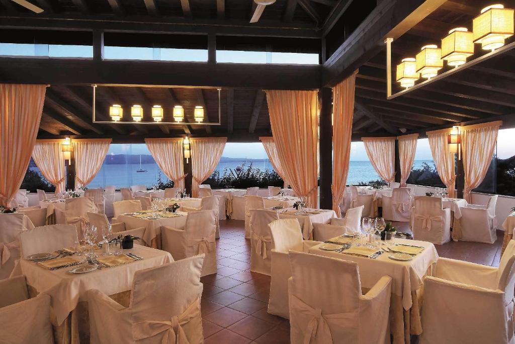 une salle de banquet avec des tables et des chaises blanches dans l'établissement COLONNA GRAND HOTEL CAPO TESTA, a Colonna Luxury Beach Hotel, Santa Teresa Sardegna, à Santa Teresa Gallura