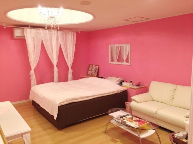 une chambre avec des murs roses et un lit et un canapé dans l'établissement Santa no Ouchi-LoveHotel, à Miyazaki 2 autres photos