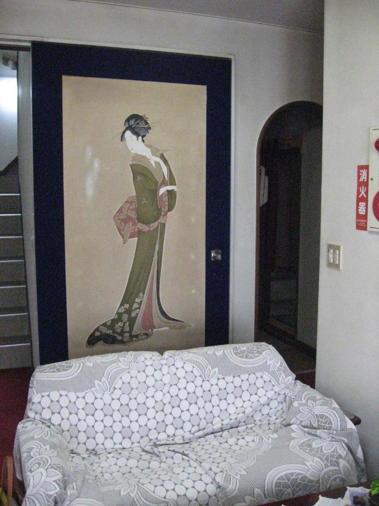 une peinture d'une femme sur un mur à côté d'un lit dans l'établissement Ichifujiso, à Fujikawaguchiko