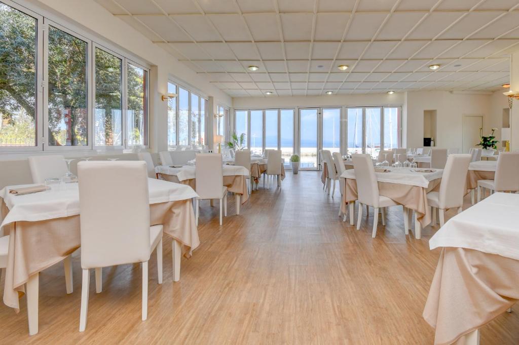un restaurant avec des tables et des chaises blanches et des fenêtres dans l'établissement VILLA GARUTI VILLAGE, à Padenghe sul Garda