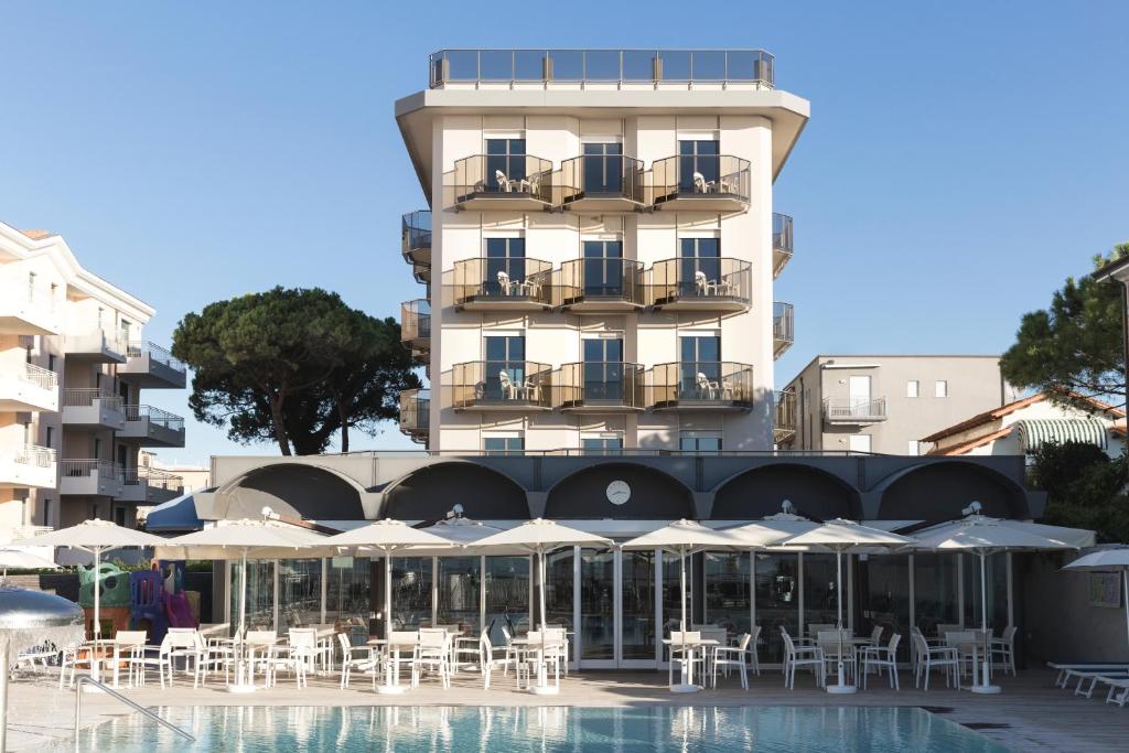 un hôtel avec des tables et des parasols à côté d'une piscine dans l'établissement Hotel Cambridge, à Lido di Jesolo