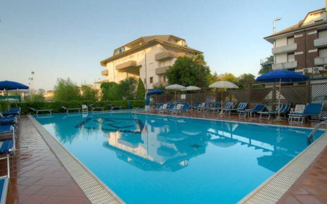 une grande piscine bleue avec chaises et parasols dans l'établissement Hotel Consuelo, à Lignano Sabbiadoro
