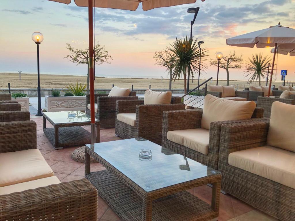 d'une terrasse avec des chaises en osier et des tables donnant sur l'océan en arrière-plan. dans l'établissement Hotel Karibe, à Bibione