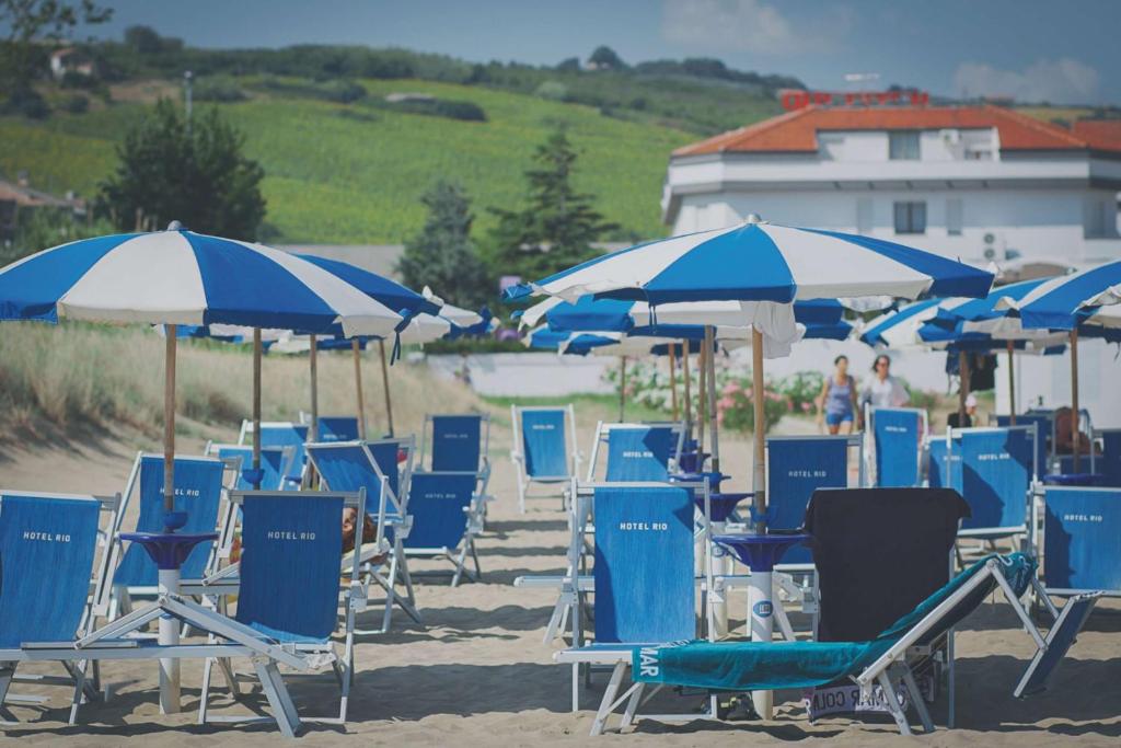 un tas de chaises bleues et de parasols sur une plage dans l'établissement Hotel Rio, à Vasto