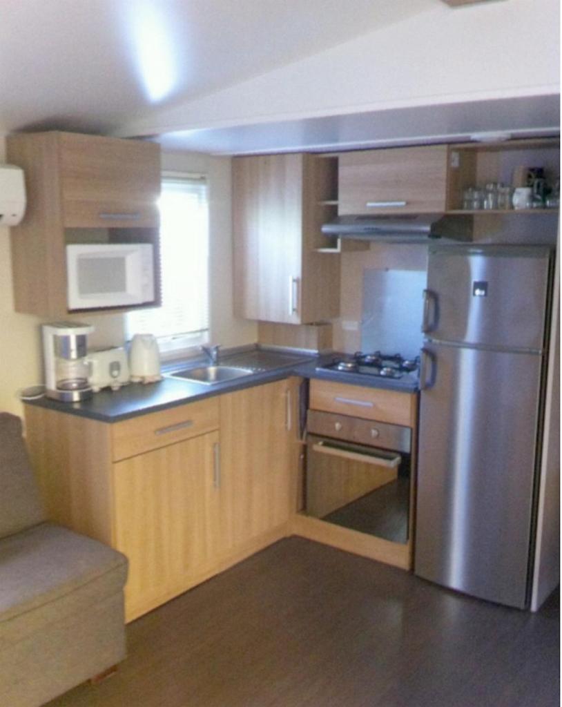 une cuisine avec des armoires en bois et un réfrigérateur en acier inoxydable dans l'établissement GRAND MOBILEHOME PROCHE COMMODITE FO10, à Fréjus