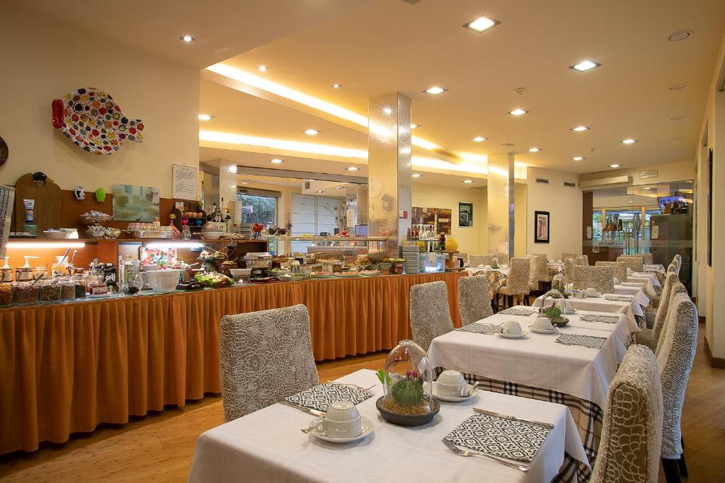 un restaurant avec des tables et des chaises blanches et un buffet dans l'établissement Hotel Daniele, à Lignano Sabbiadoro