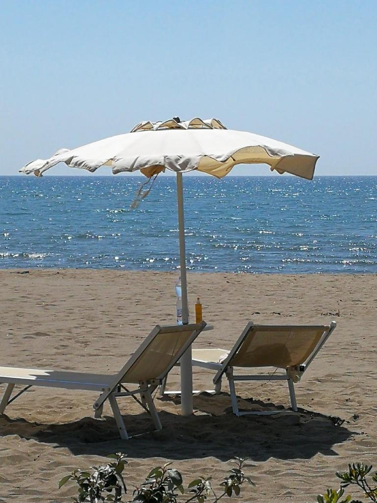 une table et des chaises sous un parasol sur la plage dans l'établissement Hotel Miramare, à Castiglione della Pescaia