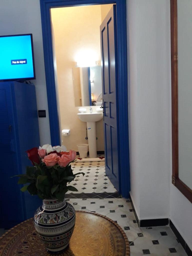 La salle de bains est pourvue d'un vase avec des roses sur une table. dans l'établissement Riad Zawia, à Essaouira