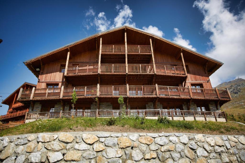 un grand bâtiment en bois au sommet d'une colline dans l'établissement CGH Résidences & Spas les Chalets du Soleil Authentiques, aux Menuires