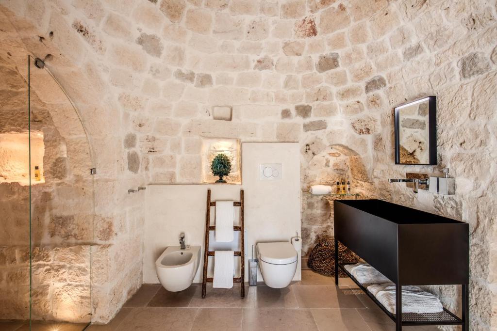 La salle de bains est pourvue d'un mur en pierre, de toilettes et d'un lavabo. dans l'établissement Lamia del Riccio, à Ostuni