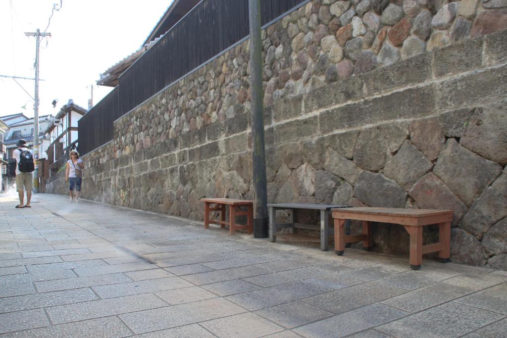 deux bancs sur un trottoir à côté d'un mur de pierre dans l'établissement Beppu Kannawa Onsen HIROMIYA, à Beppu