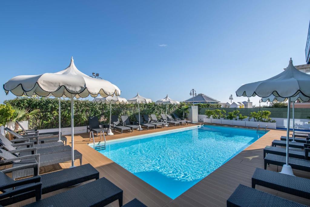une piscine avec chaises et parasols dans un hôtel dans l'établissement Hotel Mondial, à Lido di Jesolo