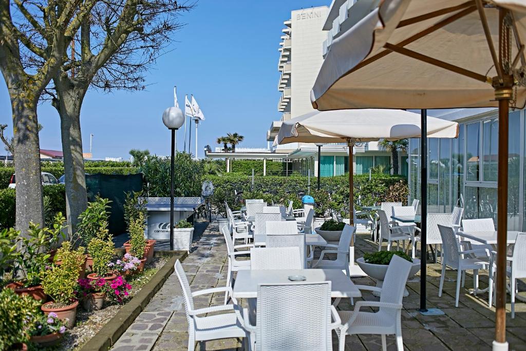 une rangée de chaises et de tables blanches ainsi qu'un parasol dans l'établissement Hotel Ridolfi, à Milano Marittima