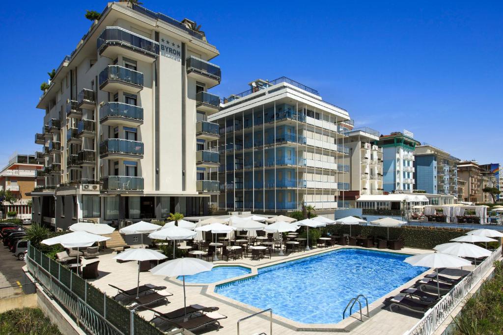un complexe avec une piscine et des parasols et un bâtiment dans l'établissement Hotel Byron Bellavista, à Lido di Jesolo