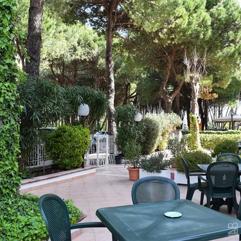 un patio extérieur avec tables, chaises et arbres dans l'établissement Hotel Admiral, à Pinarella