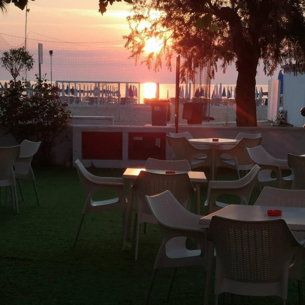 un groupe de tables et de chaises avec le coucher de soleil en arrière-plan dans l'établissement Hotel Palmarosa, à Roseto degli Abruzzi